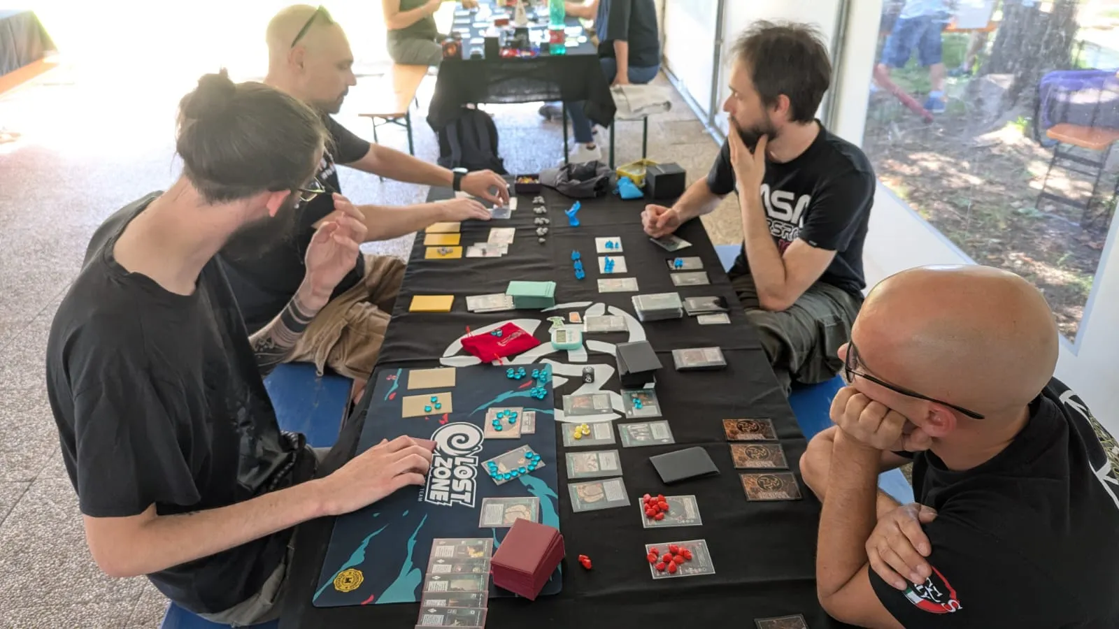 Quattro giocatori a un tavolo sotto il tendone, con un altro tavolo in gioco sullo sfondo